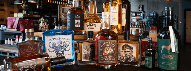 Eine Auswahl verschiedener Spirituosenflaschen, darunter Whisky und Rum, die in einem schwach beleuchteten Geschäft auf Holzregalen präsentiert werden.