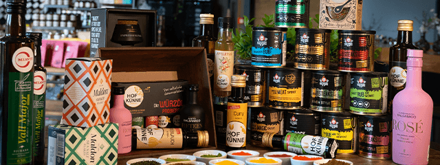 Eine Auswahl verschiedener Gourmetprodukte, darunter Öle, Saucen, Gewürzgläser und Essige mit farbenfroher Verpackung, arrangiert auf einer Ladentheke.