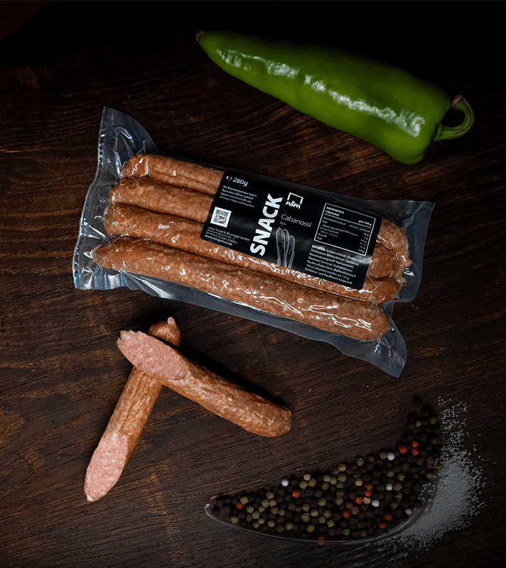 Verschiedene rohen Wurstwaren, eine grüne Paprika, Pfefferkörner und Salz auf dunklem Holzuntergrund.
