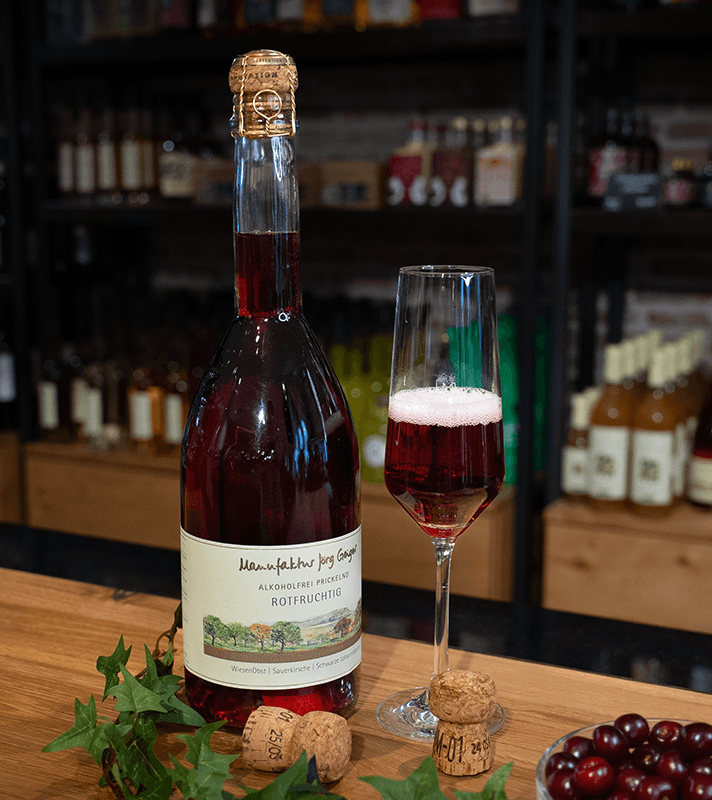 Brennender Rotwein in einer Flasche mit Korkverschluss, daneben ein Glas mit rotem Wein, Weintrauben und weitere Korken auf einem Holztablett.