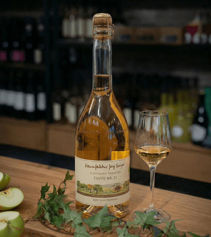 Flasche Wein mit Glas auf Holztisch, im Hintergrund Weinregal, umgeben von grünen Weinblättern.