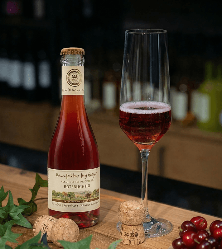 Flasche Wein mit Glas auf Holztisch, im Hintergrund Weinregal, umgeben von grünen Weinblättern.