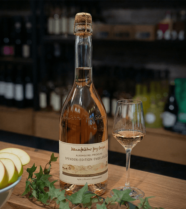 Flasche Wein mit Glas auf Holztisch, im Hintergrund Weinregal, umgeben von grünen Weinblättern.