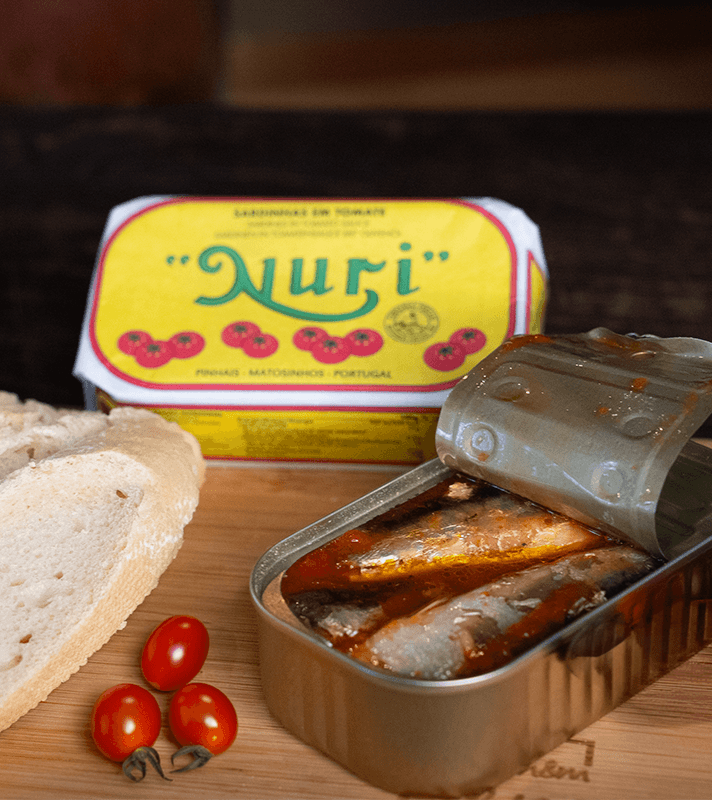 Dosen mit Sardinen in Tomatensoße, frisches Baguette, drei Cherrytomaten und eine Seife mit gelbem Etikett im Hintergrund.
