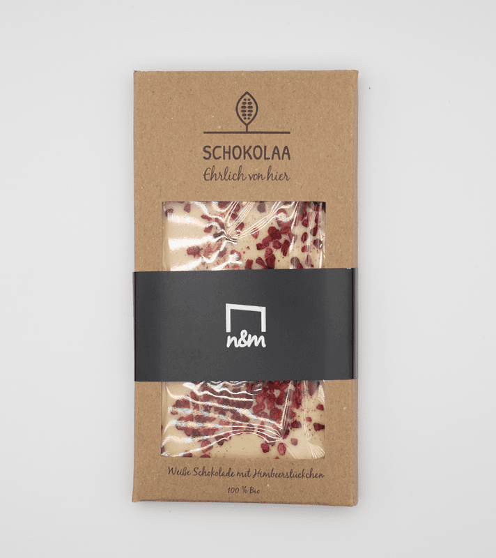 Weiße Schokolade mit Himbeerstückchen, verpackt in einer braunen Pappschachtel mit transparentem Sichtfenster.